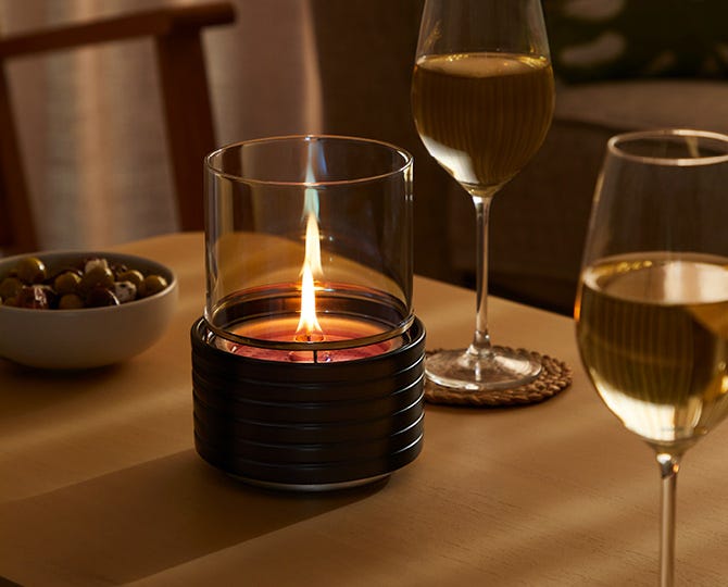 A lit Flameless Fragrance warmer on a table with two wine glasses and a bowl of olives